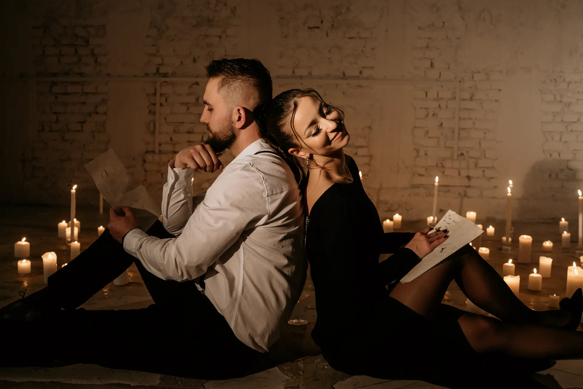 Zakochani siedzący plecami do siebie, czytający listy w otoczeniu świec.