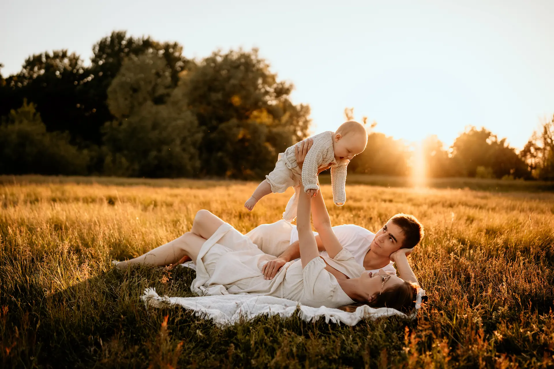 Rodzina z dzieckiem na kocu w polu podczas zachodu słońca – fotografia rodzinna Poznań
