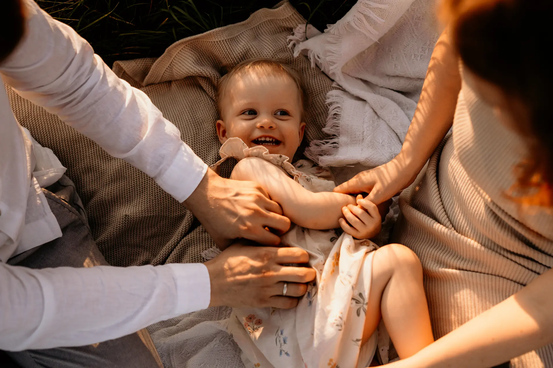 Fotografia rodzinna w Poznaniu – radosne dziecko bawiące się z rodzicami na kocu
